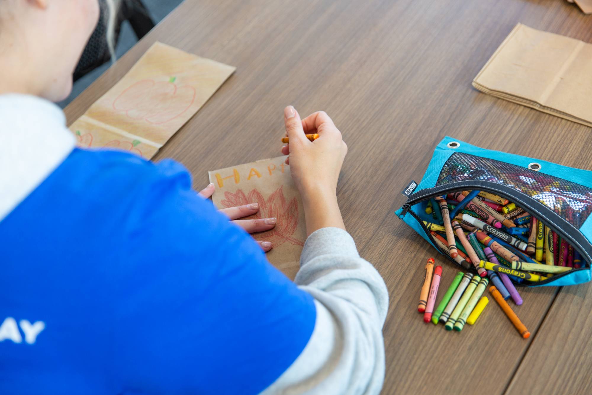 Student decorating a paper lunch bag with crayons